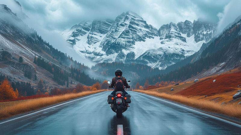 Man riding a motorcycle towards snowy mountains